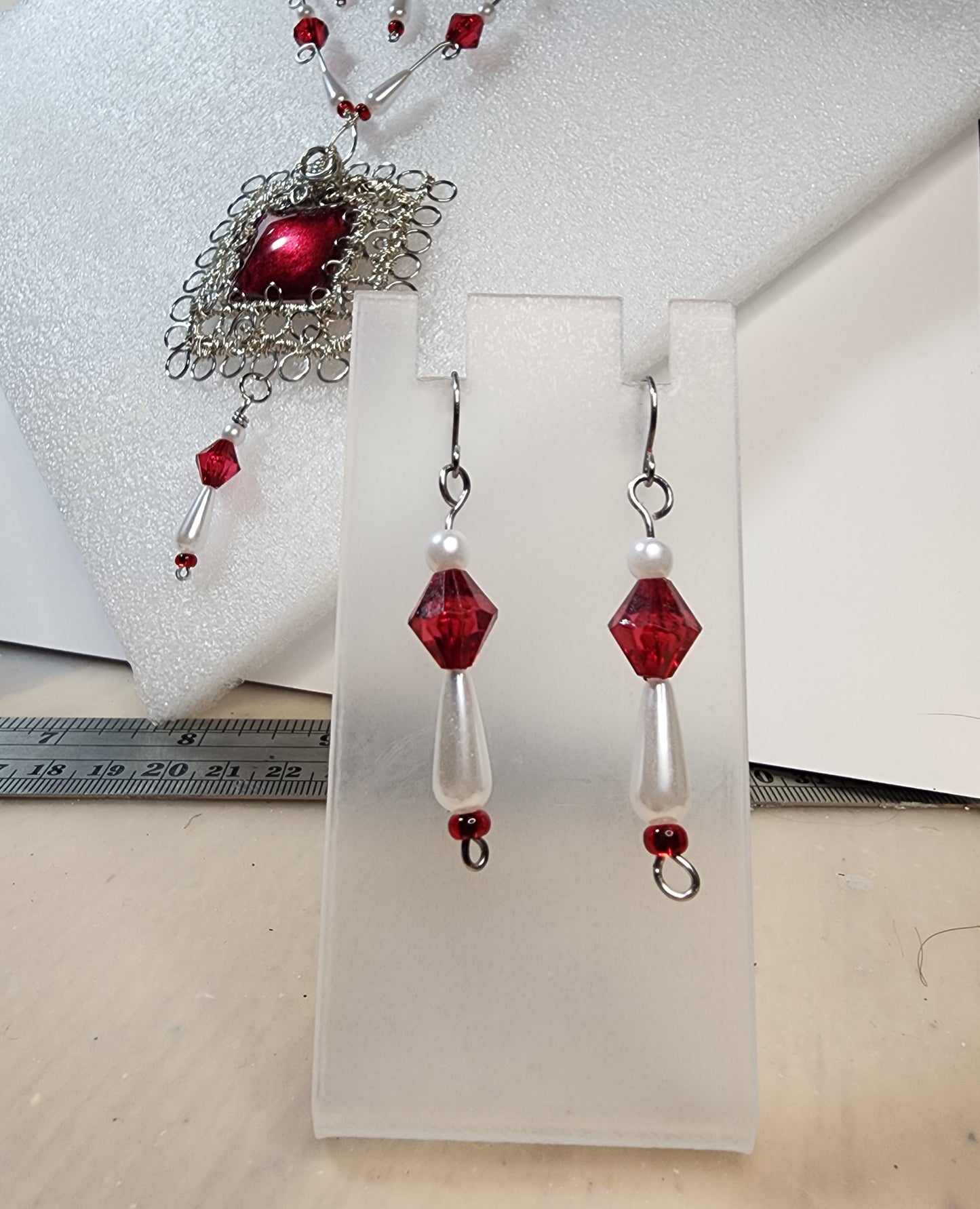 Red and faux pearl earrings on white card with red and silver pendant in the background,